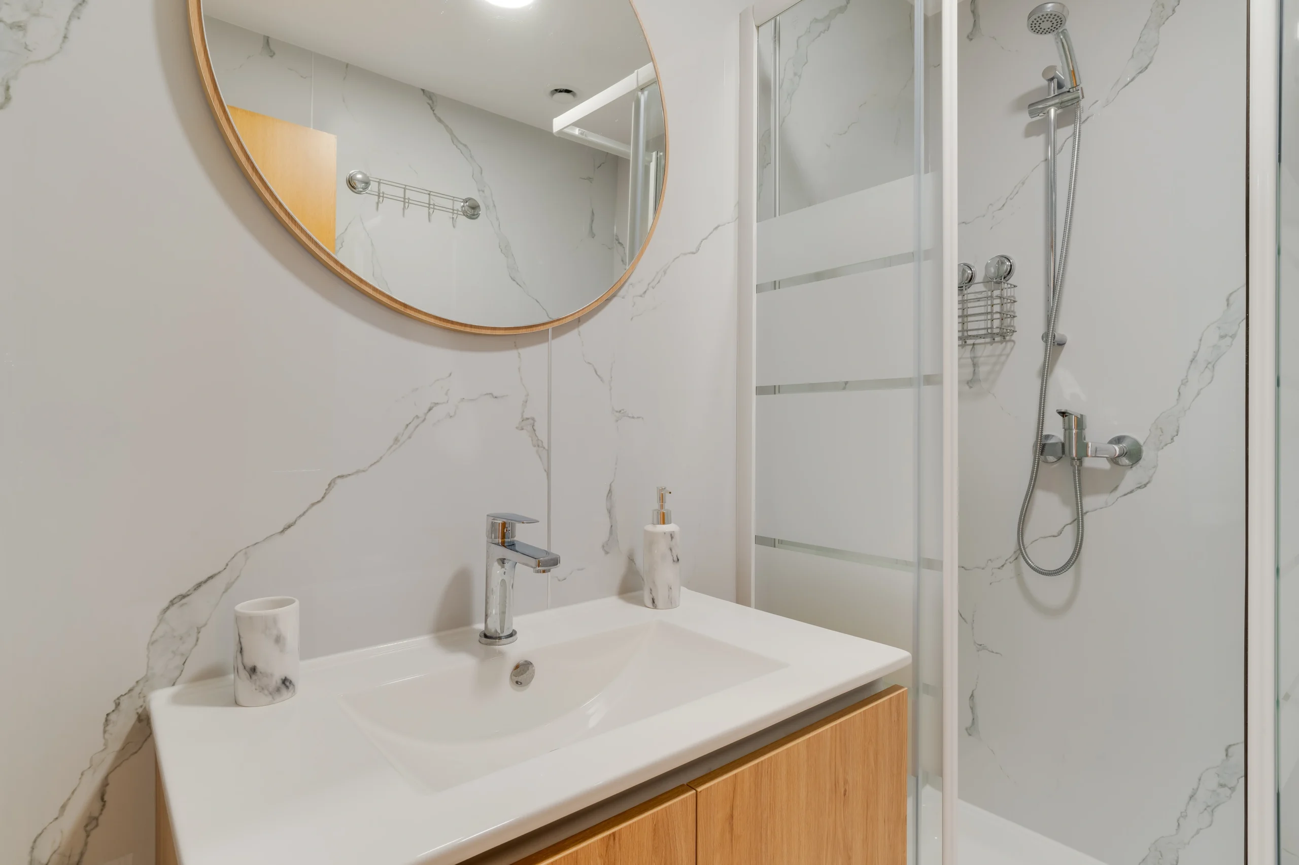 Łazienka z prysznicem, okrągłym lustrem i drewnianą szafką.