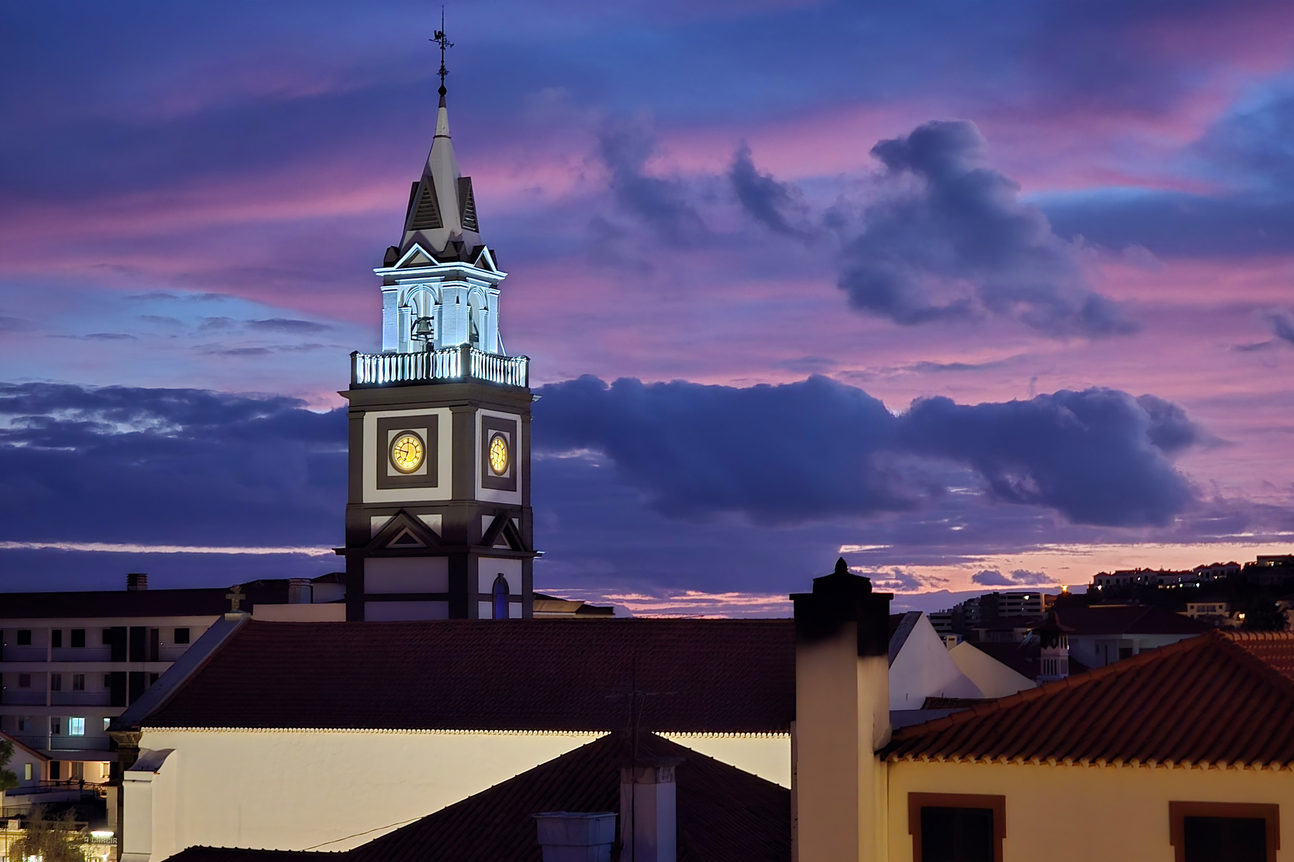 Widok z balkonu mieszkania na wieżę kościoła w Caniço oraz wielobarwny zachód słońca.