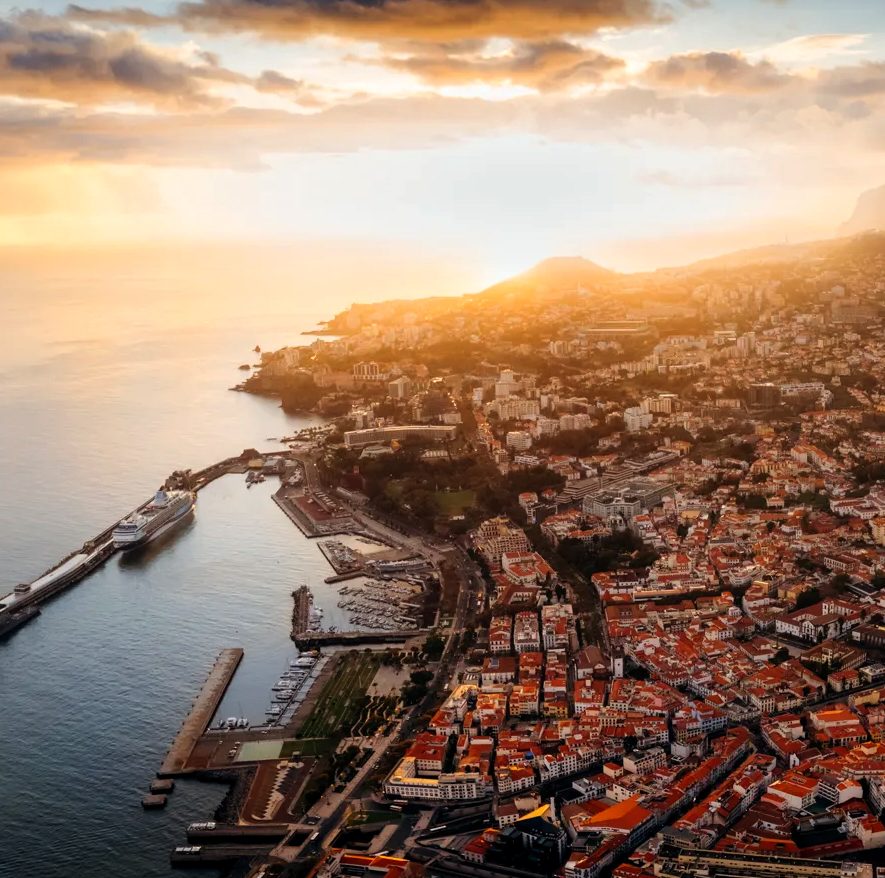 Panorama Funchal o zachodzie słońca, z gęstą zabudową miasta i górami w tle.